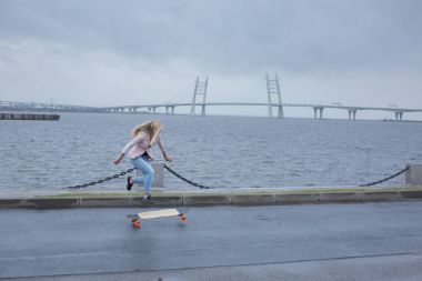 Güzel genç kız onun longboard th yakınındaki yolda sürme