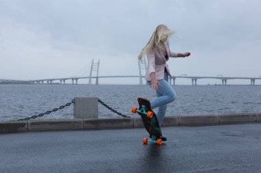 Güzel genç kız onun longboard th yakınındaki yolda sürme