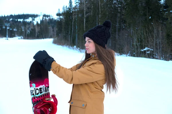 Linda chica con una tabla de snowboard en la estación de esquí —  Fotos de Stock