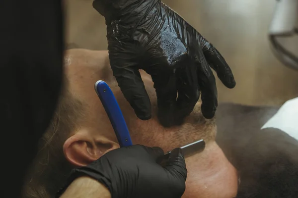 Szczegóły przycinania. Golenie brody klientowi w salonie fryzjerskim — Darmowe zdjęcie stockowe