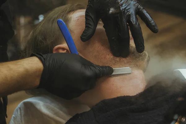Szczegóły przycinania. Golenie brody klientowi w salonie fryzjerskim — Zdjęcie stockowe