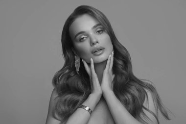 Dalgalı saçlı, güzel, genç bir esmerin siyah beyaz portresi. Yüzünde temiz deri olan güzel bir kadın. Güzellik, kozmetik ve kozmetik. Aksesuar olarak moda küpeleri