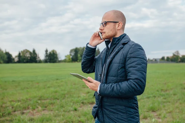 Joven inversor está sosteniendo una tableta PC mientras habla por teléfono — Foto de Stock