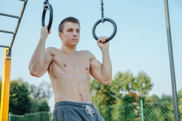 El hombre está parando en la barra. Fondo de gimnasio al aire libre — Foto de Stock