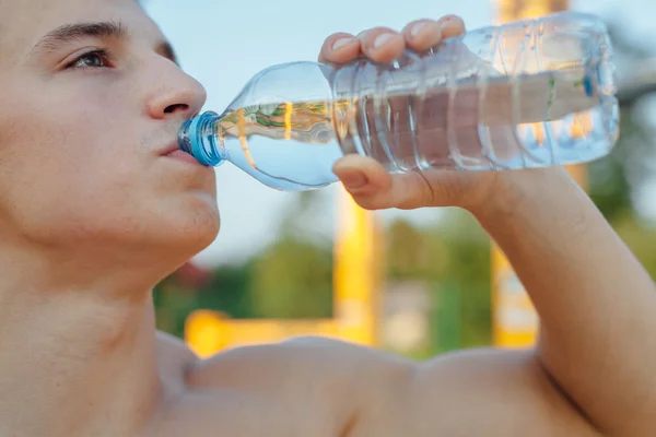 De mens is drinkbaar water na training. Outdoor sportschool achtergrond — Stockfoto