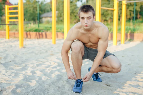 El hombre está atando el cordón de los zapatos mientras está parado en la arena. Ba gimnasio al aire libre —  Fotos de Stock