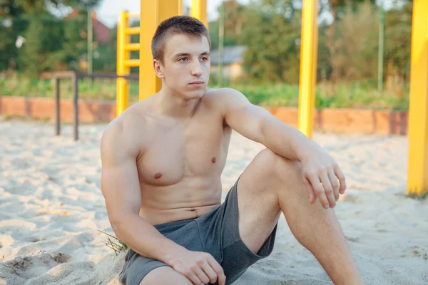 Człowiek siedzi i odpoczynku po treningu na piasku. Gy odkryty — Zdjęcie stockowe
