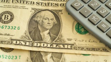 Dolar banknotları ve hesap makinesi masanın üzerinde duruyor.