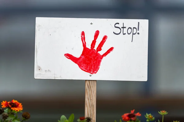 Sign with painted red hand is stuck in a flowerbed with the english inscription STOP