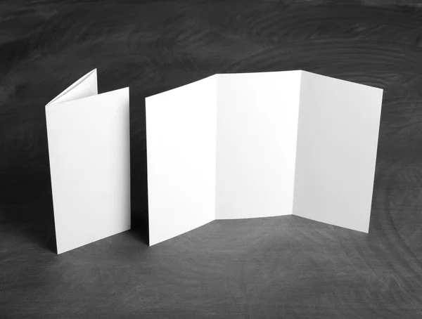 Folheto de papel dobrável branco em branco em um quadro preto — Fotografia de Stock