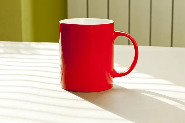 Caneca vermelha em pé sobre uma mesa contra a parede como pano de fundo . — Fotografia de Stock