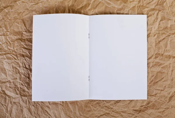 Brochure vierge ouverte sur un fond de papier ridé brun . — Photo