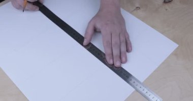 Erkek el, kağıt yaprağına kalem ve metal cetvelle bir çizgi çekiyor.