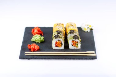 Çubuklu, zencefilli ve wassabi 'li suşi seti, açık arkaplanda siyah kare bir tabakta.. 