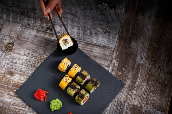 Sushi Ustawione Kwadratowej Czarnej Płytce Kamienia Samica Trzyma Rolkę Pałeczek — Zdjęcie stockowe