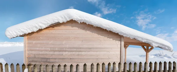 Holzblockhaus mit schneebedecktem Dach und Gitterzaun — Stockfoto