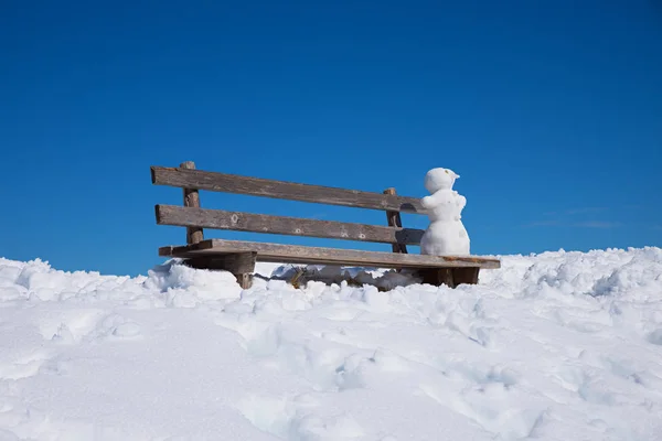 Träbänk med liten snögubbe, blå himmel — Stockfoto