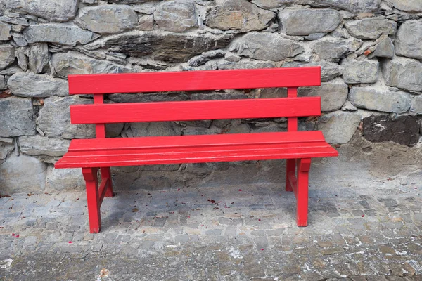 Red painted wooden bench standing on a stone pavement, rough wal — Stock Photo, Image