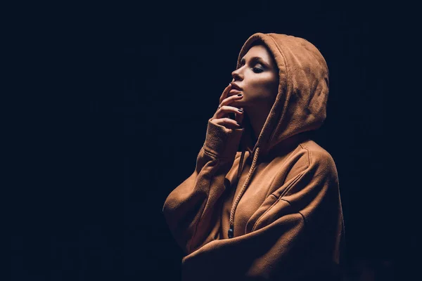 Studio portrait of a girl in a hoodie on a dark background — Stock fotografie