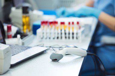 Barkod tarayıcı, kan örneği tüpleri ve laboratuvar teknisyeninin elleri arka planda. Coronavirus COVID-19 Laboratuar Analizi İş Yeri.