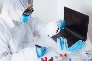 Koruyucu maske, kan örneği tüpleri ve laboratuvar teknisyenlerinin elleri arka planda. Coronavirus COVID-19 Laboratuar Analizi İş Yeri.