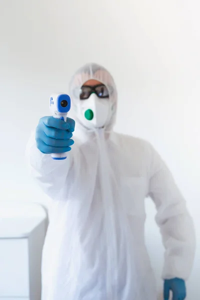 Doctor sosteniendo termómetro infrarrojo. Retrato del profesional médico en ropa protectora que mide la fiebre sin contacto en el centro de pruebas Covid-19 durante la epidemia de coronavirus . — Foto de Stock