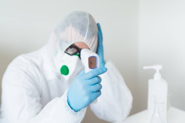 Tıbbi profesyoneller koronavirüs risk kavramı. Ateşli, koruyucu giysili bir doktor hastanede Covid-19 için kendini ölçüyor..