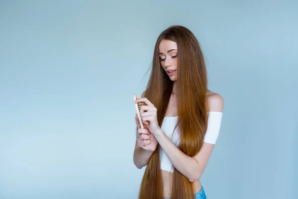 Concept of hair loss. Close up portrait of unhappy sad stressed young woman with long dry brown hair, she is looking at the brush in hand, isolated on grey background. — Stock Photo, Image