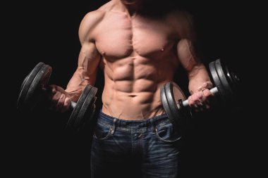 Dambılı olan yakışıklı atletik adam kendinden emin bir şekilde ileriye bakıyor. Güçlü vücut geliştirici, karın kasları, omuzları, pazıları, trisepsleri ve göğsü var. Kuvvet ve motivasyon