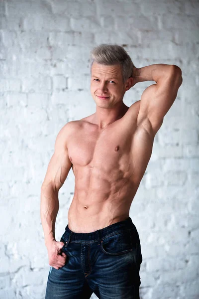 Portrait d'un homme musclé torse nu dans un jean. Jeune homme beau gosse montrant son corps parfait et ses muscles sur fond de brique blanche . — Photo