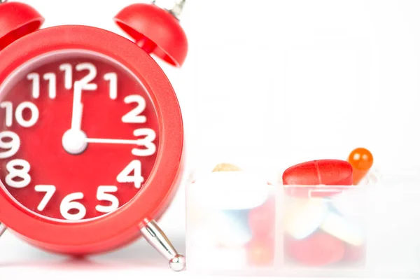 Reloj despertador rojo y caja de pastillas muestran concepto de medicina — Foto de Stock