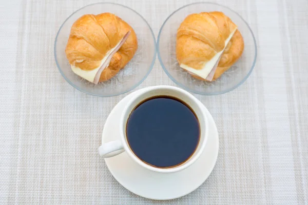 Uma xícara de café preto com presunto e croissant de queijo — Fotografia de Stock