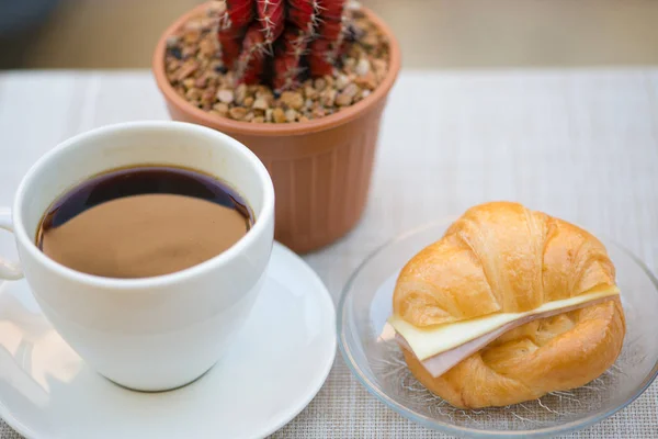 Uma xícara de café preto com presunto e croissant de queijo — Fotografia de Stock