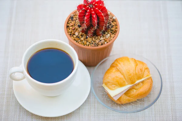 Uma xícara de café preto com presunto e croissant de queijo — Fotografia de Stock