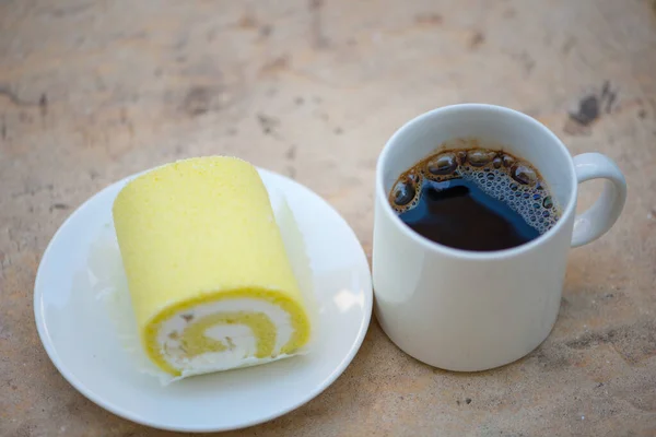 Black coffee and Sponge cake cream roll on white dish show bakery background