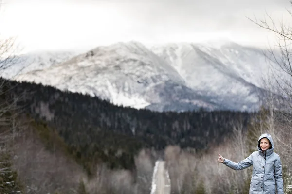 Mulher Hitchhiking em uma estrada de inverno com montanhas — Fotografia de Stock