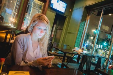 Montreal, Kanada - 30 Kasım 2017: bir restoran bir Smartphone ile St-Denis Street, Montreal'de arka plan üzerinde bir adres için geceleri kontrol kadın.