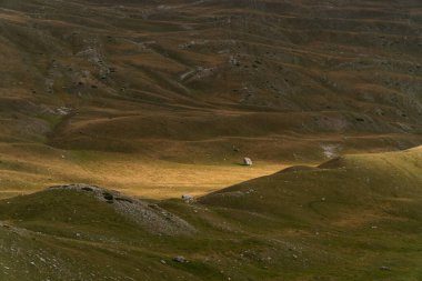 Dağların eteğindeki yeşil tepeler gün batımında güneş ışınlarıyla aydınlatılıyor.