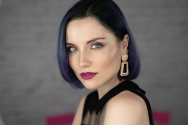 Profesyonel makyajlı, mavi saçlı ve mükemmel ciltli genç bir kız stüdyoda sosyal medya için poz veren bir lambanın önünde oturuyor. Güzellik blogu. Boşluğu kopyala.