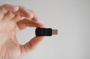 Adam elinde USB bellek tutuyor. Parmak uçları beyaz bir arka planda.