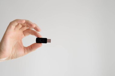 Adam elinde USB bellek tutuyor. Parmak uçları beyaz bir arka planda.