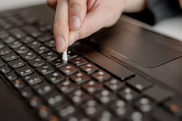 A man cleans a keyboard with a cotton swab and an antiseptic. Dirty place. Danger of bacterial and virus infection