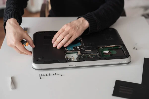 A man disassembles a laptop. Computer service and repair concept. Laptop disassembling in repair shop, close-up. Electronic development, electronic device fixing