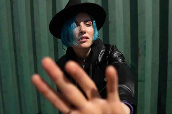 A girl in a black hat and a leather jacket is trying to grab the camera.