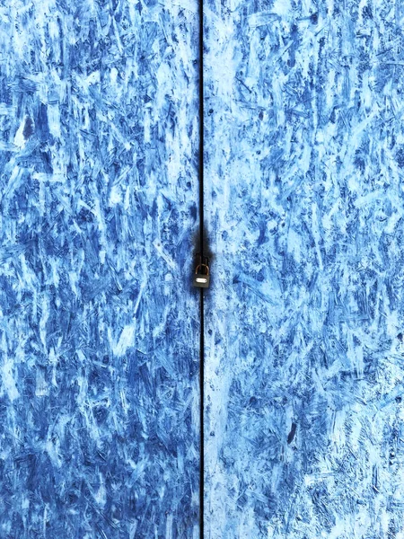 An old garage door with lock, blue colored, made of pressed chipboard wood, background texture. Close-up view