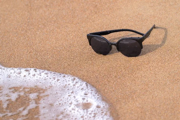 Sunglasses and sandy coast with wave — Stock Photo, Image