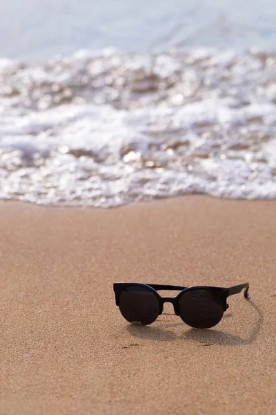 Солнечные очки и песчаное побережье с волной — стоковое фото