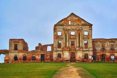 Boş yeşil bir çayırda harap olmuş eski tuğla binaların kalıntıları ve boş ve temiz gökyüzünün arka planı.