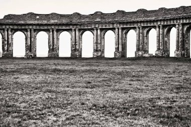 Boş yeşil bir çayır üzerinde eski tuğla kemerli duvarların antik kalıntıları ve boş ve temiz arkaplandaki tek renkli ton gökyüzü