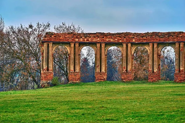 ancient ruins of old brick arched walls on an empty green meadow and against the background of empty and clean sky